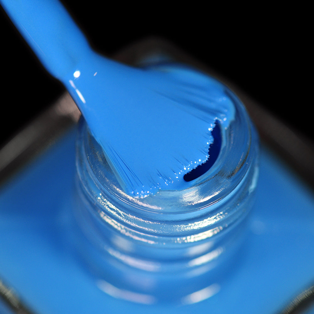 Close-up of a nail polish brush coated in vibrant blue Bored Meeting nail polish, positioned above the open neck of a matching blue bottle against a black background.
