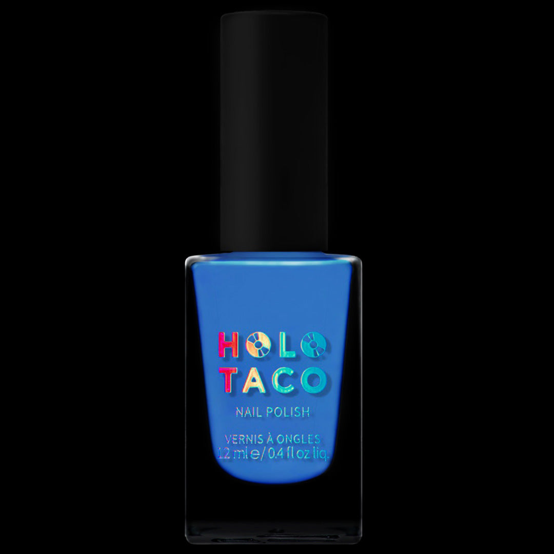 A bottle of Holo Taco nail polish in the shade Bored Meeting features a bright blue color, a black cap, and a label with the brand name in holographic letters, all set against a black background.